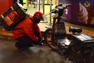 A McDonalds delivery man unlocks his rusty, taped-up scooter for his next route.